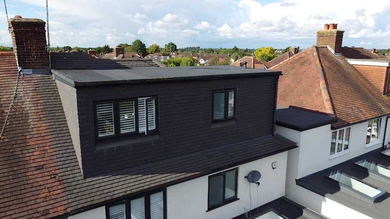 Full-width rear dormer in dark cladding against a clear sky
