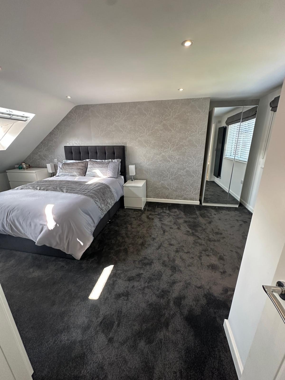 Sunlit loft bedroom with mirrored wardrobe and grey carpet