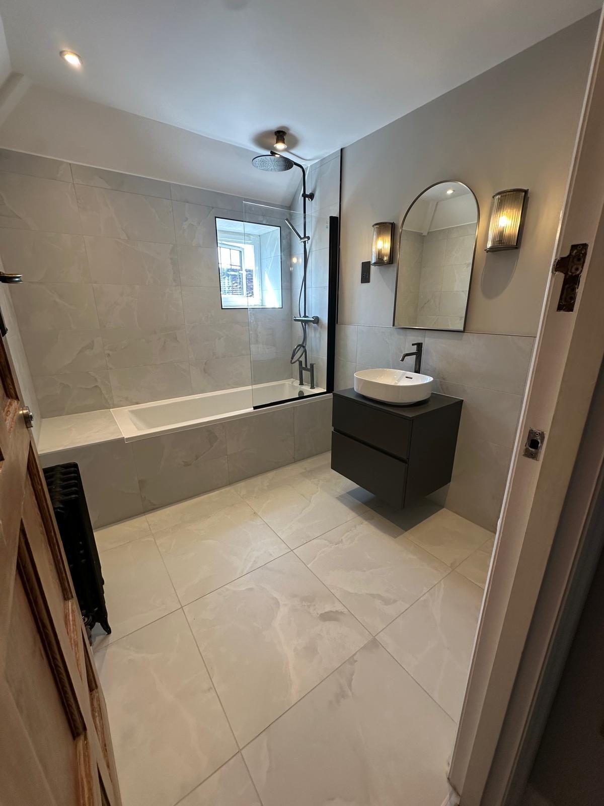 Stone-tiled bathroom with black-framed bath screen and arched mirror, Banstead